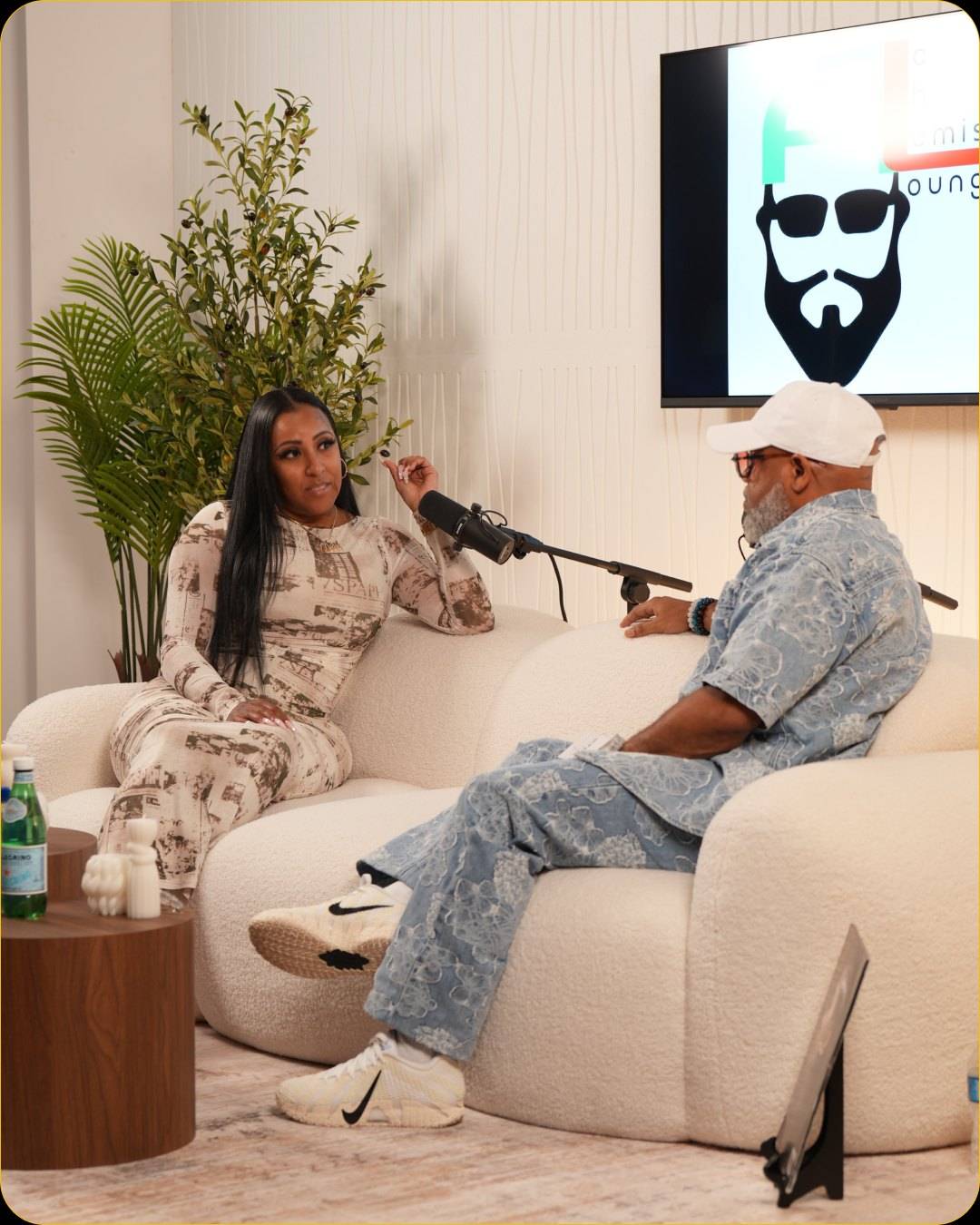 Two guests talking on the white sofa of Studio #2 into boom-arm microphones, with a show logo on the wall display