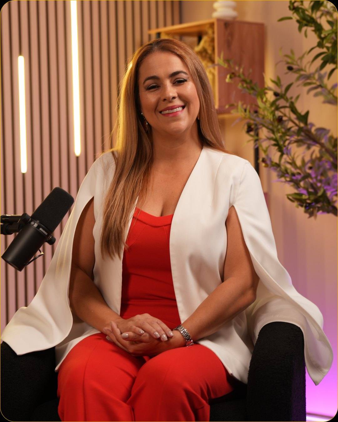 A guest in a white blazer and a red outfit at the microphone in Studio #3, with LED light bars behind her