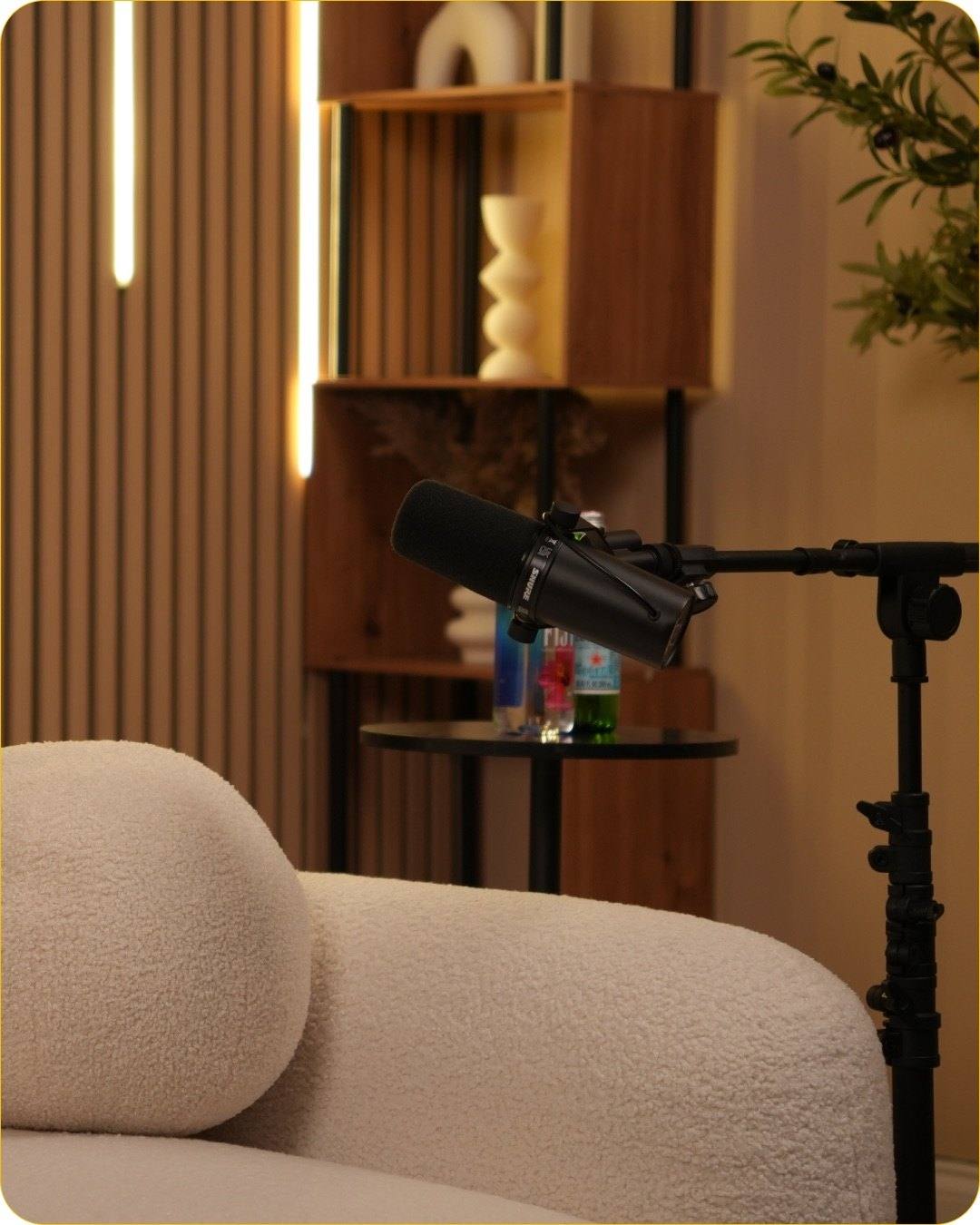 A podcast microphone on a boom arm beside the white sofa of Studio #5, with LED light bars on the wall behind it