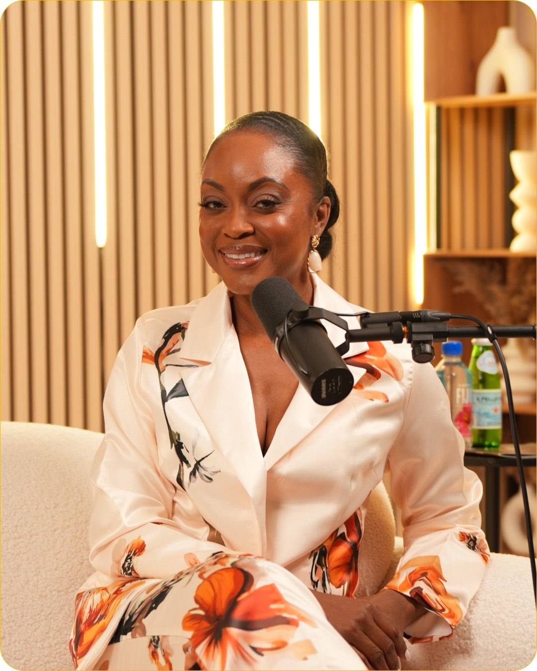 A smiling guest in a white blazer with an orange floral print at the microphone on the sofa of Studio #5