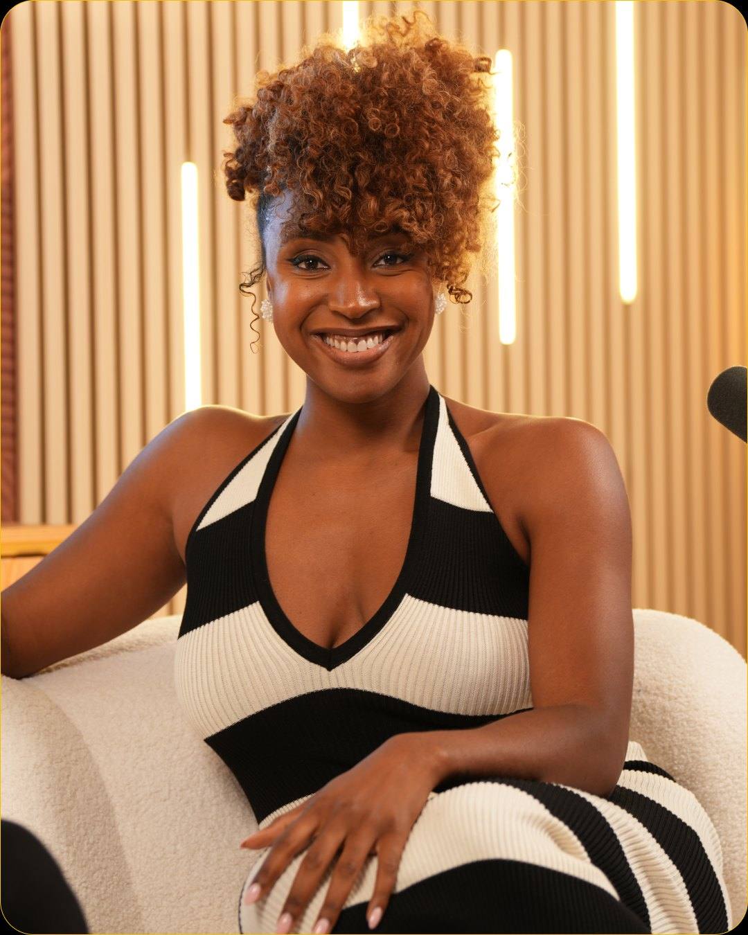 A smiling guest in a black and white striped top on the white sofa of Studio #5, with the wood slat wall and LED light bars behind her
