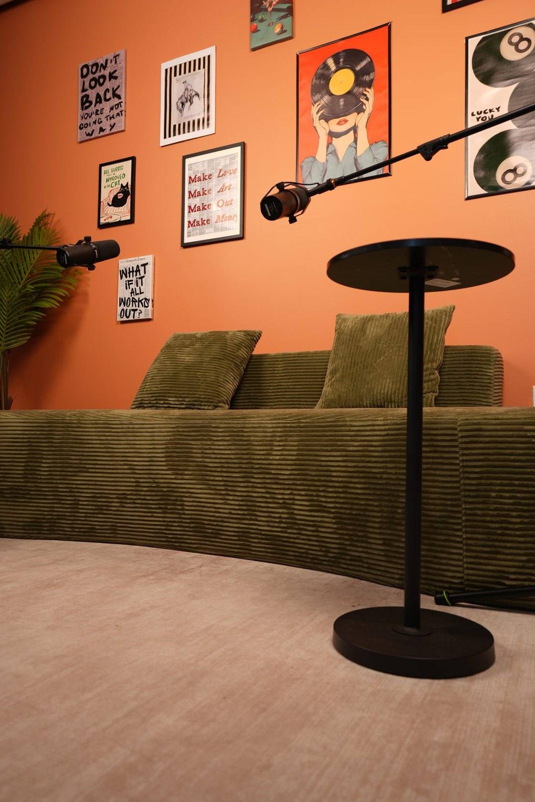Studio #6 at The Cast Studio: two microphones on boom arms by a green corduroy sofa against an orange wall